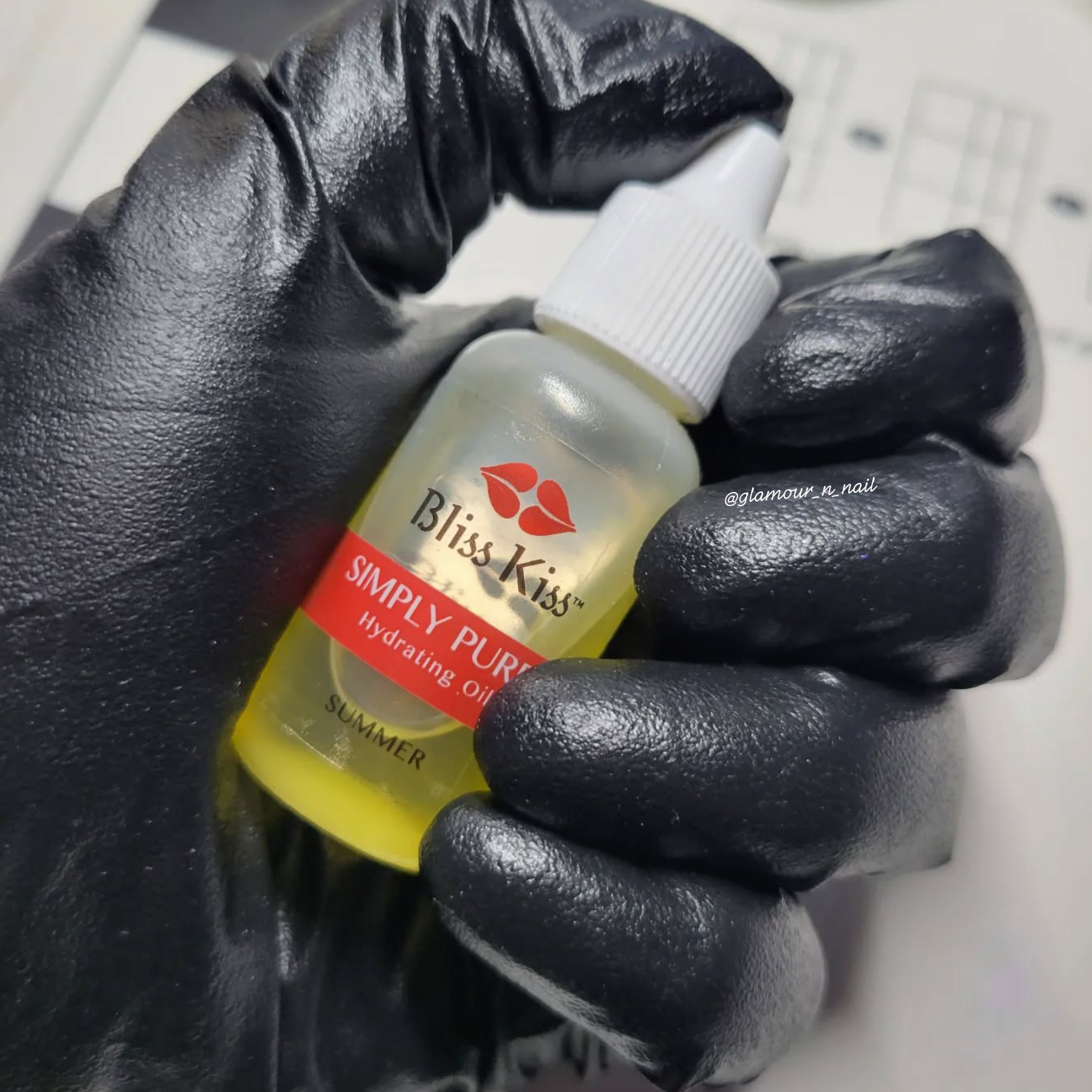 Hand holding a bottle of 'Bliss Kiss Simply Pure' product with a black glove.